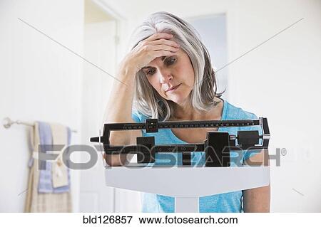 Stock Photo - Unhappy Caucasian woman standing on weight scale. Fotosearch