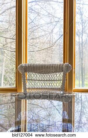 Picture - Window behind wicker chair and glass table. Fotosearch
