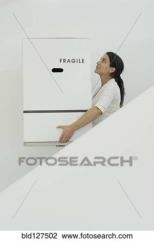 Stock Image - Woman carrying boxes downstairs side view. Fotosearch