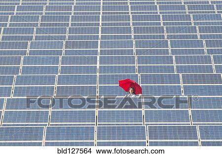 Picture - woman holding red umbrella in solar power plant. Fotosearch