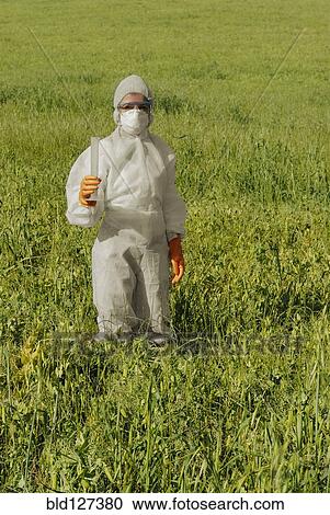 Stock Image - Woman in boiler suit standing in field holding test tube. Fotosearch