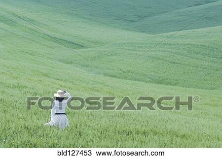 Stock Image - Woman in white dress walking through rolling hills of young wheat. Fotosearch