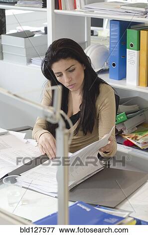 Stock Photo - woman reading documents at her desk in office. Fotosearch