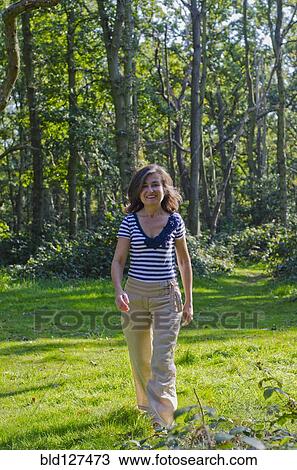 Stock Image - woman walking across clearing in forest. Fotosearch