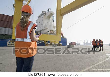 Woman wearing hard hat holding clipboard standing on dockside View Large Photo Image Stock Image - Woman wearing hard hat holding clipboard standing on dockside. Fotosearch
