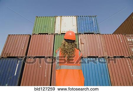 Woman wearing hard hat standing by containers in dock rear view View Large Photo Image Stock Photo - Woman wearing hard hat standing by containers in dock rear view. Fotosearch