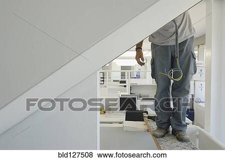 Stock Photo - Workman installing electric cabling in new office low section. Fotosearch