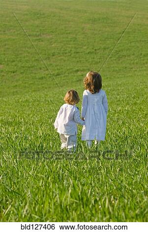 Stock Photograph - Young brother and sister holding hands in field rear view. Fotosearch