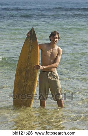 Young surfer standing in water holding surfboard portrait View Large Photo Image Stock Photograph - Young surfer standing in water holding surfboard portrait. Fotosearch