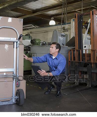Stock Photograph - Caucasian businessman examining boxes in warehouse. Fotosearch