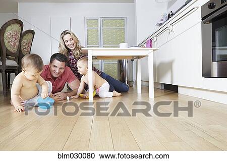 Stock Image - Caucasian family playing on kitchen floor. Fotosearch
