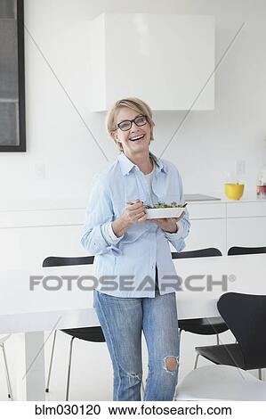 Stock Image - Caucasian woman eating in kitchen. Fotosearch