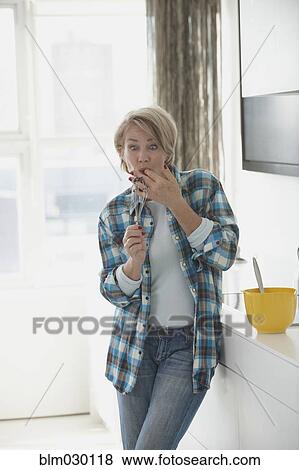 Stock Photo - Caucasian woman licking whisk n kitchen. Fotosearch