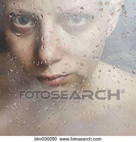Stock Image - Caucasian woman peering through wet glass. Fotosearch