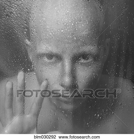 Stock Image - Caucasian woman peering through wet glass. Fotosearch