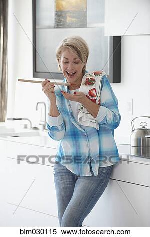 Stock Photography - Caucasian woman tasting food in kitchen. Fotosearch