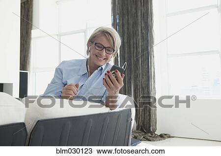 Stock Image - Caucasian woman using cell phone on sofa. Fotosearch