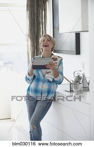 Stock Photograph - Caucasian woman using digital tablet in kitchen. Fotosearch