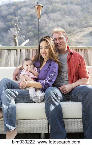 Stock Image - Family smiling on patio sofa. Fotosearch