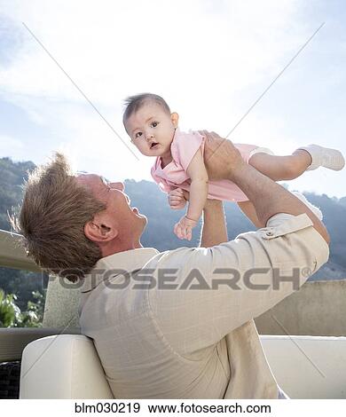 Stock Photo - Father holding baby girl on sofa. Fotosearch