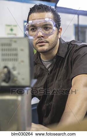 Picture - Hispanic worker operating machinery in factory. Fotosearch