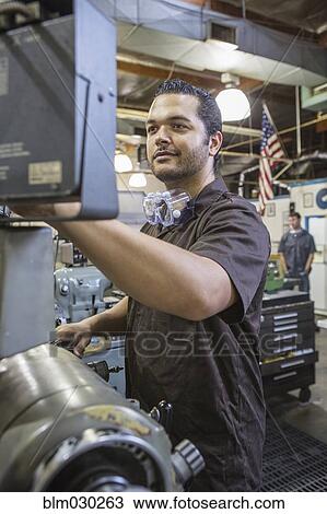Stock Image - Hispanic worker operating machinery in factory. Fotosearch