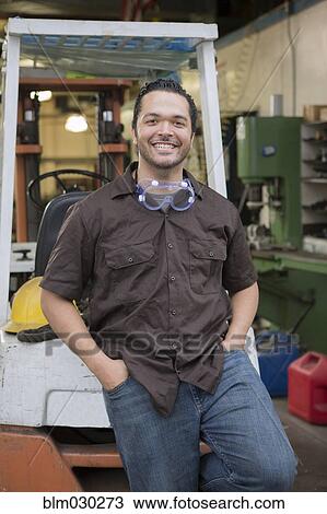 Stock Image - Hispanic worker smiling in warehouse. Fotosearch