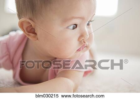 Stock Photography - Mixed race baby girl laying on carpet. Fotosearch