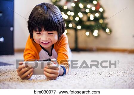 Stock Photo - Mixed race boy playing with smart phone in living room. Fotosearch