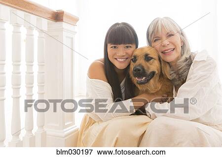 Stock Photo - Mother and daughter hugging dog on steps. Fotosearch