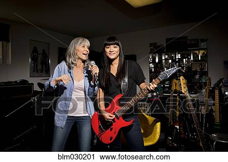 Stock Image - Mother and daughter singing and playing guitar in basement. Fotosearch