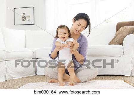 Picture - Mother helping baby girl stand in living room. Fotosearch