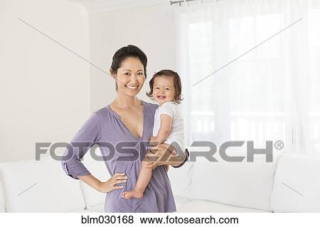 Stock Photo - Mother holding baby girl in living room. Fotosearch