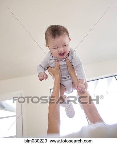 Stock Photo - Mother holding baby girl overhead. Fotosearch