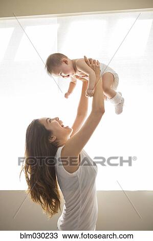 Stock Image - Mother lifting baby girl overhead. Fotosearch