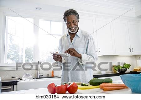 Picture - Senior man using digital tablet in kitchen. Fotosearch