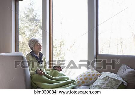 Picture - Senior woman meditating on sofa. Fotosearch