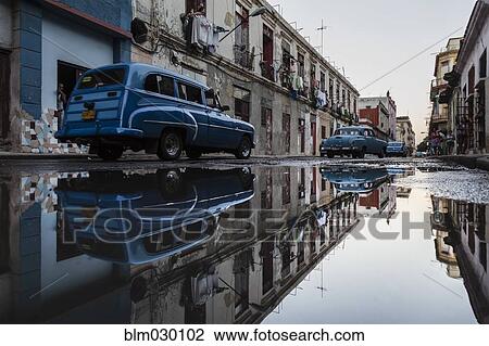 Stock Image - Vintage cars reflected in puddles on La Habana street, Havana, Cuba. Fotosearch