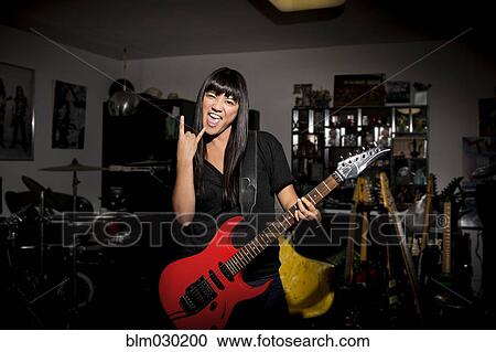 Stock Image - Woman playing electric guitar in basement. Fotosearch