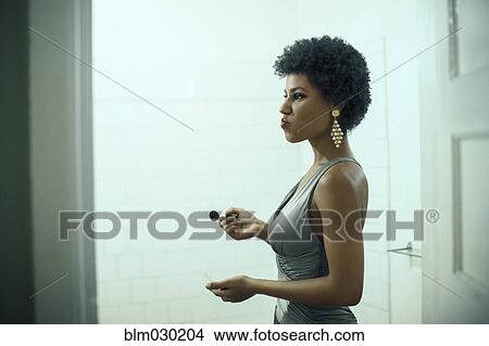 Picture - Woman putting on makeup in bathroom. Fotosearch