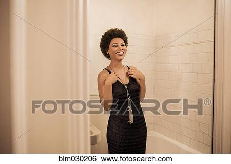 Stock Photograph - Woman putting on necklace in bathroom. Fotosearch