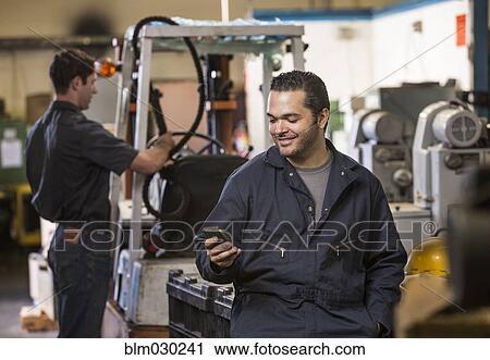 Stock Image - Worker using cell phone in warehouse. Fotosearch