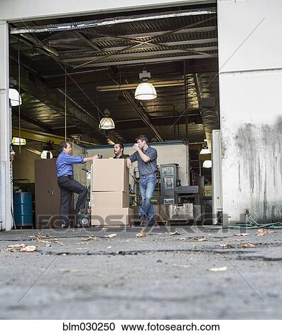 Stock Image - Workers enjoying coffee break at warehouse loading dock. Fotosearch