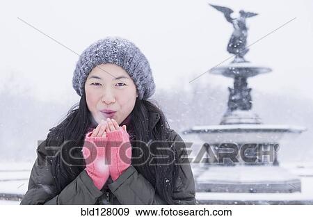 Stock Photo - Asian woman blowing on hands in snow. Fotosearch