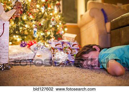 Stock Image - Caucasian boy sleeping by Christmas gifts. Fotosearch