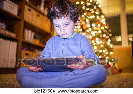 Caucasian boy using digital tablet by Christmas tree View Large Photo Image Picture - Caucasian boy using digital tablet by Christmas tree. Fotosearch