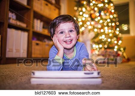 Stock Image - Caucasian boy using digital tablet by Christmas tree. Fotosearch