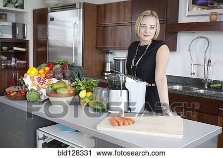 Stock Image - Caucasian businesswoman juicing in kitchen. Fotosearch