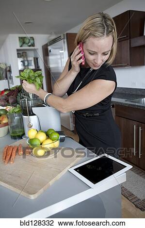 Stock Image - Caucasian businesswoman juicing in kitchen. Fotosearch