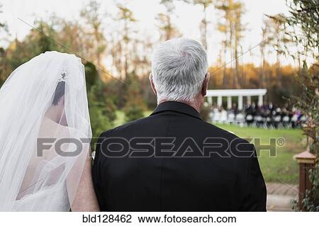 Stock Image - Caucasian father walking bride down aisle. Fotosearch